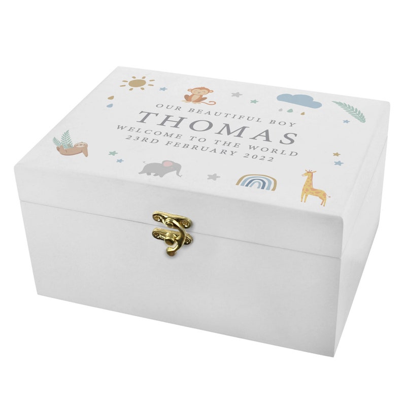 May include: White wooden keepsake box with a gold-colored clasp. The lid features the text "OUR BEAUTIFUL BOY THOMAS WELCOME TO THE WORLD 23RD FEBRUARY 2022" and illustrations of a sun, monkey, cloud, sloth, elephant, rainbow, giraffe, and stars.