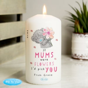 Puede incluir: Una vela blanca en forma de pilar con un oso de peluche gris que sostiene una flor rosa. La vela tiene el texto "Si las mamás fueran flores, te elegiría" y "De Grace" impreso en ella.