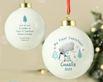 May include: Two white Christmas ornaments with gold caps and red ribbons. One ornament has a blue Christmas tree graphic and text. The other ornament has a teddy bear, penguin, and bunny graphic with the text "My First Christmas" and a name and year.