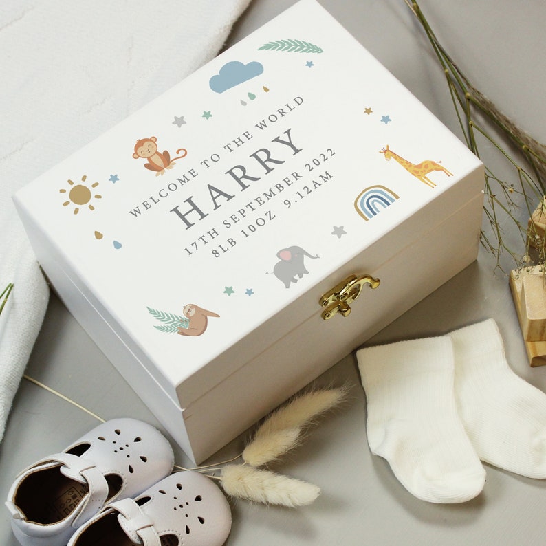 May include: A white wooden keepsake box with a gold clasp, decorated with baby-themed illustrations. The box is personalized with the name "HARRY", birthdate, and weight. Baby shoes and socks are next to the box.