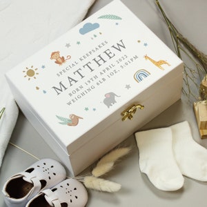 May include: A white keepsake box with a gold clasp, decorated with a monkey, giraffe, elephant, and sloth. The box is personalized with the name "MATTHEW", birth date, and weight. Baby shoes and socks are next to the box.