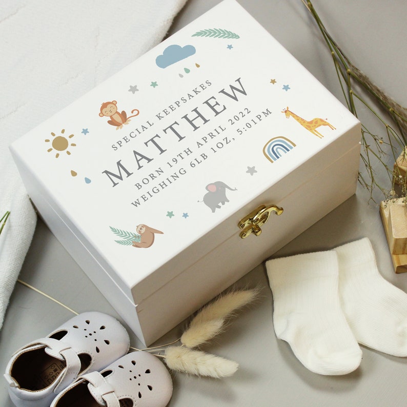 May include: A white keepsake box with a gold clasp, decorated with a monkey, giraffe, elephant, and sloth. The box is personalized with the name "MATTHEW", birth date, and weight. Baby shoes and socks are next to the box.