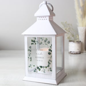 May include: White lantern with a clear glass panel featuring a eucalyptus wreath and a personalised message that reads "Emily and George 14-10-23".