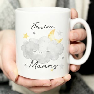 Puede incluir: Taza de cerámica blanca con una ilustración de acuarela de una nube gris con una cara dormida, una luna creciente amarilla y estrellas amarillas. El texto "Jessica Mummy" está impreso en la taza.