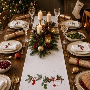 May include: A white linen table runner featuring embroidered green pine branches, red bows, and colorful stockings. The runner is centered on a wooden dining table set with white plates, crystal glasses, gold cutlery, and a festive centerpiece.