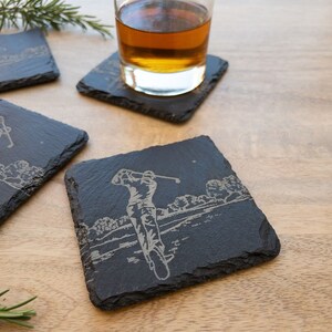 Può includere: Set di quattro sottobicchieri in ardesia nera con un design a silhouette di golfista. I sottobicchieri sono quadrati e hanno una texture ruvida e naturale.