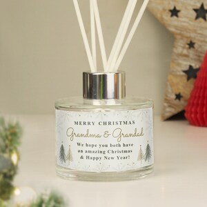May include: A clear glass reed diffuser bottle with a silver cap and white reeds. The label features a snowflake pattern, gold text reading Merry Christmas Grandma & Grandad, and the message We hope you both have an amazing Christmas & Happy New Year.