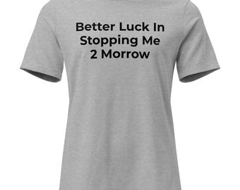 May include: A light gray short-sleeved t-shirt featuring the black printed text Better Luck In Stopping Me 2 Morrow centered on the chest. The garment has a crew neckline and a standard fit, showcasing a simple design with clear, bold lettering.