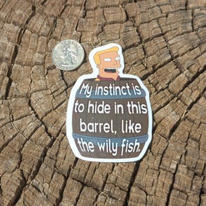 May include: A sticker featuring a cartoon character inside a brown barrel with the text "My instinct is to hide in this barrel, like the wily fish." A quarter is next to the sticker.