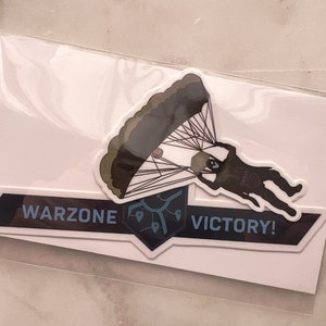 May include: A black and blue sticker with a white outline. The sticker features a cartoon image of a person parachuting with the text "Warzone Victory!"