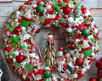 May include: A Christmas wreath decorated with red, green, and white ornaments, candy canes, and a snowman figurine. The wreath is made of a variety of materials, including faux flowers, berries, and pine cones.