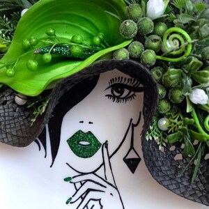 Pode incluir: Um chap&eacute;u preto e verde com uma flor verde e um rosto de mulher com l&aacute;bios verdes e esmalte de unha verde. O rosto da mulher &eacute; desenhado em preto e branco.