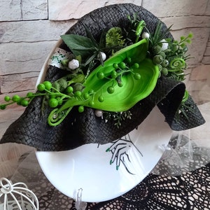 Pode incluir: Um chap&eacute;u preto tecido com detalhes florais verdes e brancos. O chap&eacute;u est&aacute; sobre um prato branco com um design em preto e branco.