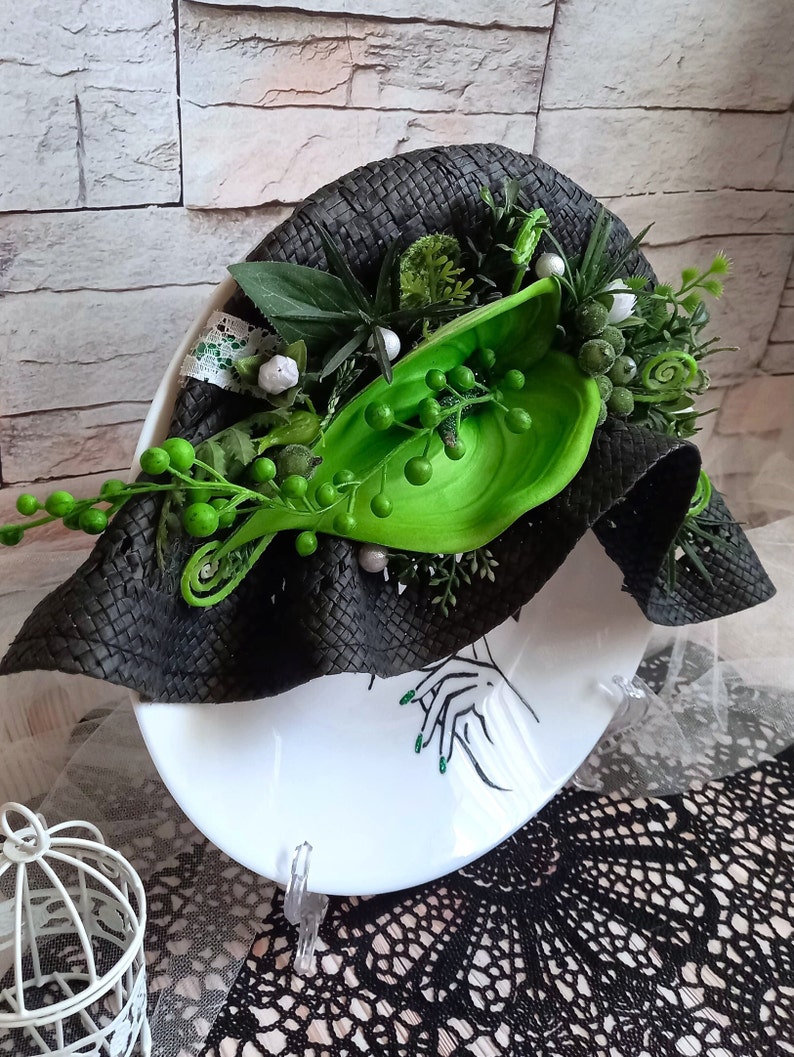 Pode incluir: Um chap&eacute;u preto tecido com detalhes florais verdes e brancos. O chap&eacute;u est&aacute; sobre um prato branco com um design em preto e branco.