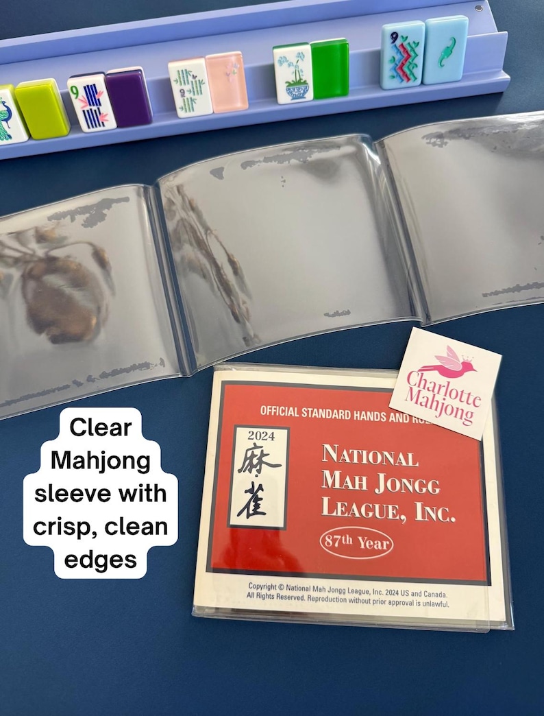 May include: A clear plastic protective sleeve for a 2024 National Mah Jongg League official hands and rules card, featuring a red cover with white text, alongside a light purple tile rack holding various colorful mahjong tiles with symbols.
