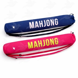 Puede incluir: Dos estuches cil&iacute;ndricos para fichas de Mahjong. Uno es azul marino con texto blanco y una correa negra. El otro es rosa intenso con texto amarillo-verdoso y una correa rosa. Ambos estuches tienen un patr&oacute;n de p&aacute;jaros.