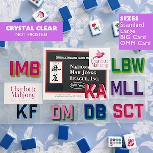 May include: A collection of clear plastic Mah Jongg card holders featuring various letter combinations like IMB, LBW, MLL, KF, DM, DB, SCT, and KA. The set includes an official 2025 National Mah Jongg League card and Charlotte Mahjong branding.