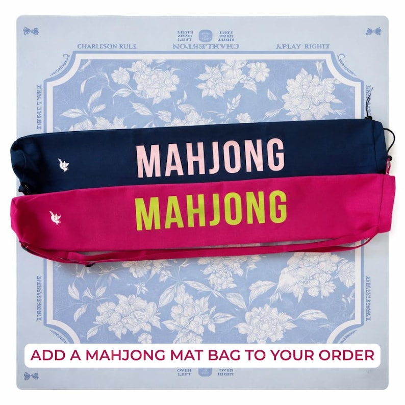 Puede incluir: Dos bolsas para tapetes de Mahjong, una azul marino y otra fucsia, se muestran sobre un tapete con estampado floral. La palabra "MAHJONG" est&aacute; impresa en letras grandes y contrastantes en cada bolsa. El texto "ADD A MAHJONG MAT BAG TO YOUR ORDER" es visible.