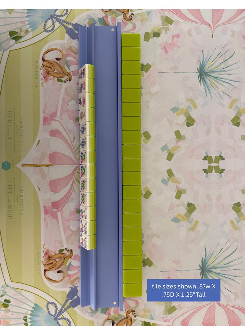 May include: A blue Mahjong tile rack with green tiles and a row of patterned tiles. The text on the image reads: "tile sizes shown .87w X .75D X 1.25"Tall". The background features a whimsical pattern with monkeys and floral designs.