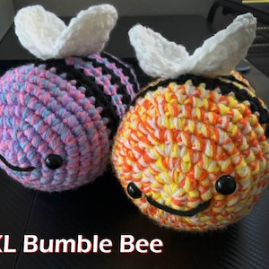 Puede incluir: Dos peluches de abejorro de crochet. Uno es rosa y azul con rayas negras, el otro es amarillo, naranja y blanco con rayas negras. Ambos tienen alas blancas de crochet y ojos negros. XL Bumble Bee.