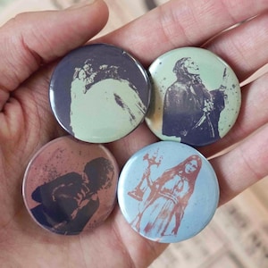 Puede incluir: Cuatro chapas redondas con siluetas oscuras de figuras sobre fondos de colores. La chapa de arriba a la izquierda es morada, la de arriba a la derecha es verde claro, la de abajo a la izquierda es marrón rojizo y la de abajo a la derecha es azul claro.