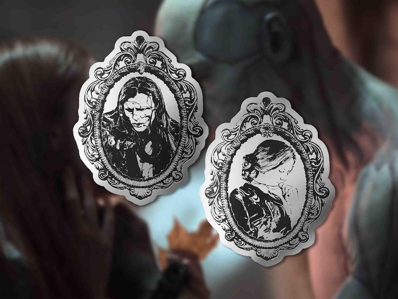 May include: Two black and white stickers featuring portraits within ornate oval frames. One depicts a person with long hair and a stern expression, the other a person with their hair up and head bowed. The stickers have a vintage aesthetic.
