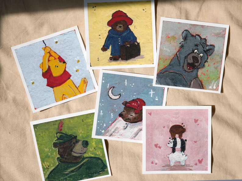 May include: A collection of six square art prints featuring bear characters in various scenes. The prints showcase illustrations of bears in different settings, including Winnie the Pooh, Paddington Bear, and others, with a whimsical and colorful style.