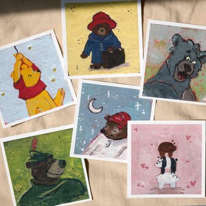 May include: A set of six illustrated cards featuring different cartoon bears. The cards are all white with a light blue, pink, or yellow background. The bears are depicted in various poses and settings, including a bear wearing a red hat and carrying a suitcase, a bear wearing a red hat and holding a moon, and a bear wearing a green hat and holding a sword.