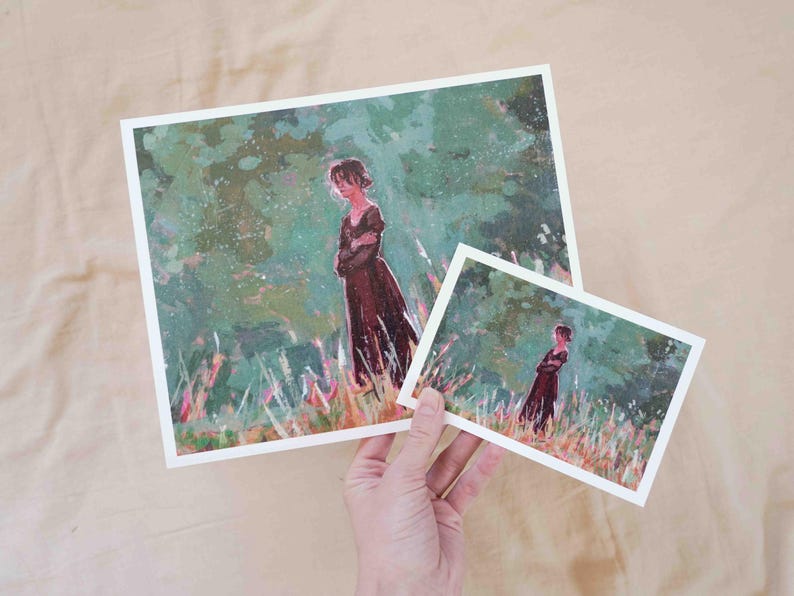 May include: Two art prints depicting a woman in a long, dark dress in a field. The larger print is held in a hand, with a smaller version visible. The artwork has a painterly style with green and brown tones.