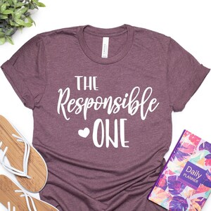 May include: A maroon t-shirt with the text "The Responsible One" in white lettering with a small heart symbol before the word "One".