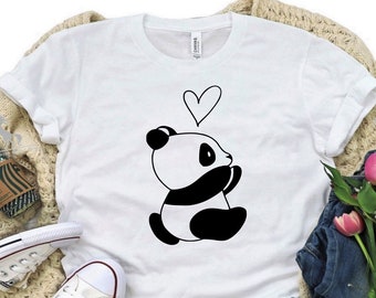 May include: White t-shirt featuring a black and white illustration of a panda bear holding a heart. The panda is sitting on a white background.