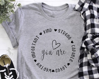 May include: Gray t-shirt with a black circle design that says "You are" with a heart in the middle and the words "important, kind, strong, capable, loved, worthy" around the circle.