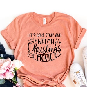 Puede incluir: Una camiseta de color melocotón con el texto "Let's bake stuff and watch Christmas movies" en letras negras.