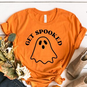 K&ouml;nnte beinhalten: Orangefarbenes T-Shirt mit einem schwarzen Geistermotiv und dem Text "Get Spooked".