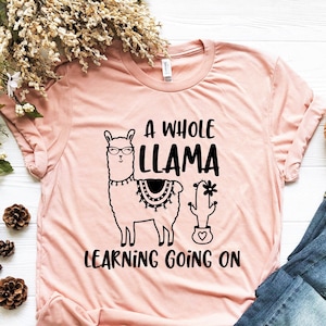 May include: A pink t-shirt with a black llama wearing glasses and a cactus with the text "A Whole Llama Learning Going On".