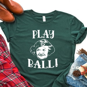 May include: A green t-shirt with white text that says "PLAY BALL!" and a picture of a woman's face.
