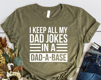 May include: A green t-shirt with white text that reads "I keep all my dad jokes in a dad-a-base".