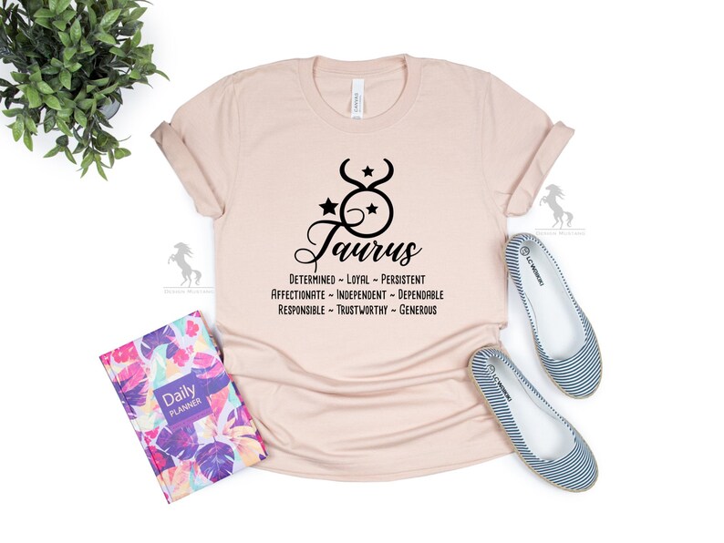 May include: A light pink t-shirt with a black Taurus zodiac symbol and the text "Taurus" in a cursive font. The text "Determined - Loyal - Persistent - Affectionate - Independent - Dependable - Responsible - Trustworthy - Generous" is printed below the symbol.