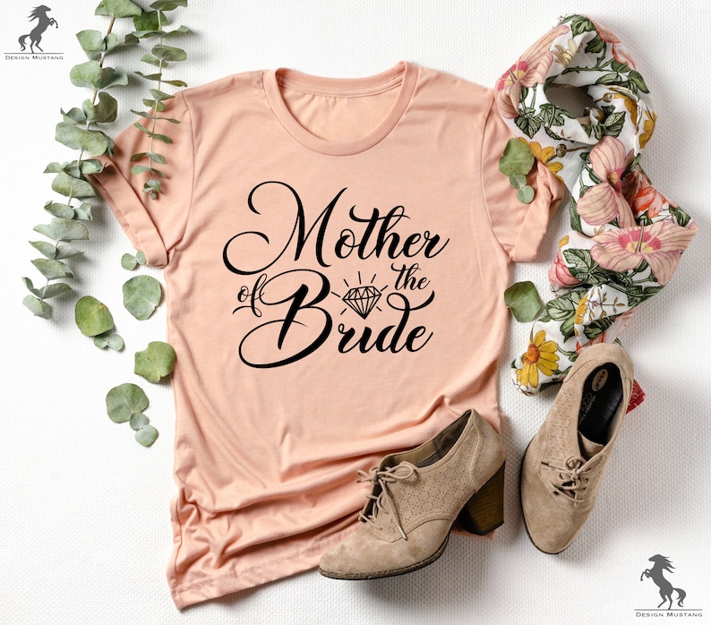 May include: A peach-coloured t-shirt with the text "Mother of the Bride" in black script with a diamond graphic above the word "Bride".