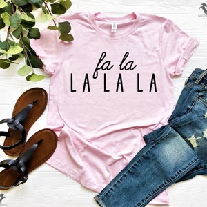 May include: A pink t-shirt with the text "fa la LA LA LA" printed in black.