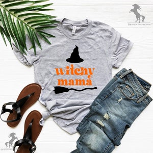 May include: A gray t-shirt with the text "witchy mama" in orange letters and a black witch's hat and broom graphic.