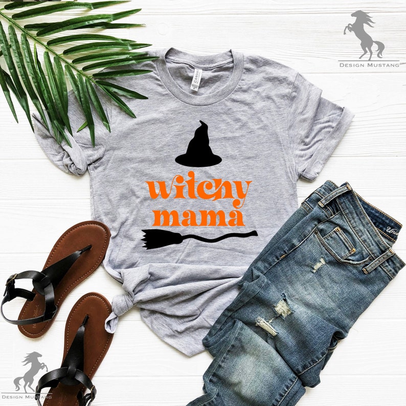 May include: A gray t-shirt with the text "witchy mama" in orange letters and a black witch's hat and broom graphic.
