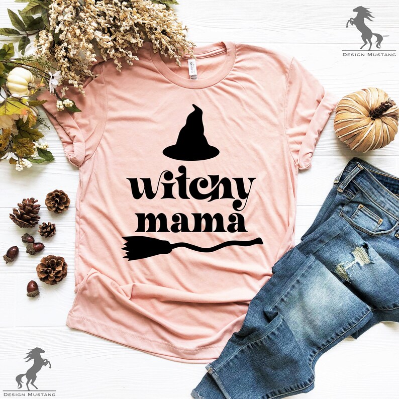 May include: A pink t-shirt with a black witch hat, broom, and the text "witchy mama" printed on it.