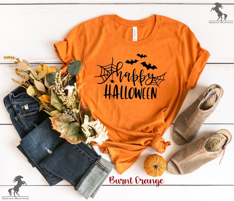 May include: Burnt orange t-shirt with a black graphic that says "Happy Halloween" with bats and a spider web.