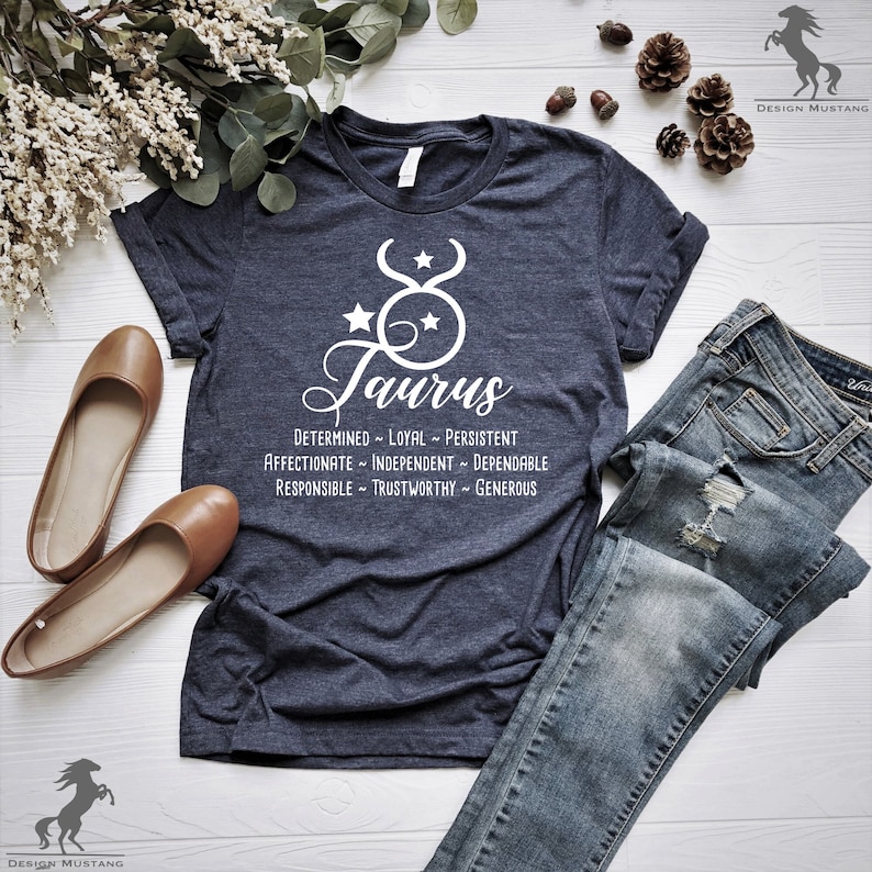 May include: A dark blue t-shirt with a white graphic of the Taurus zodiac sign and the word "Taurus" written below. The graphic also includes two stars. The text below the graphic lists the traits of a Taurus: "Determined - Loyal - Persistent, Affectionate - Independent - Dependable, Responsible - Trustworthy - Generous."