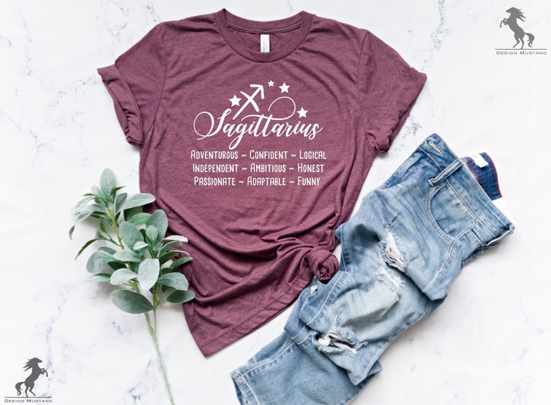 May include: A maroon t-shirt with a white graphic of the Sagittarius zodiac sign and a list of personality traits: adventurous, confident, logical, independent, ambitious, honest, passionate, adaptable, and funny.