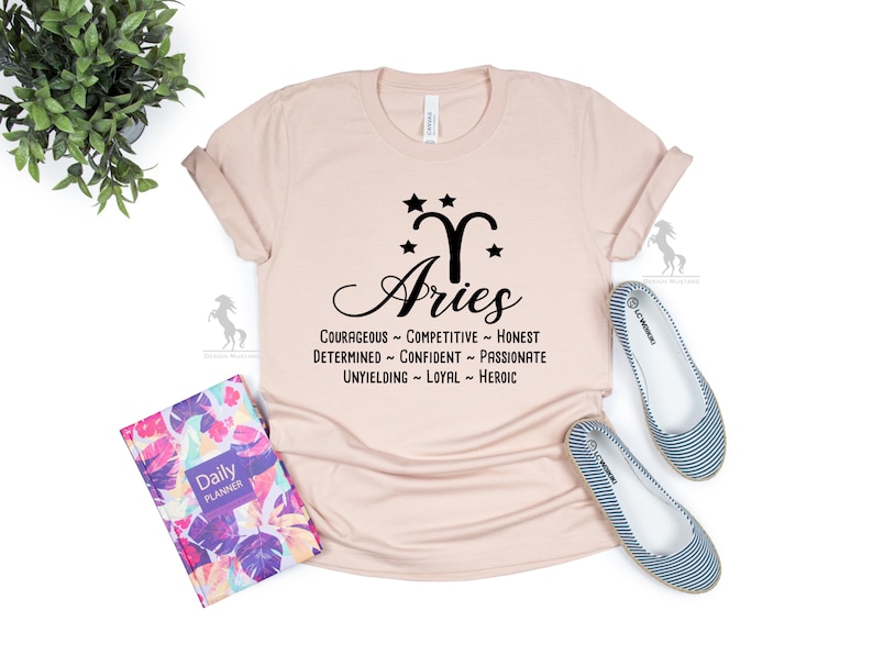 Może przedstawiać: Jasnor&oacute;żowy T-shirt z czarną grafiką przedstawiającą znak zodiaku Baran ze gwiazdami i słowem "Baran" pisanym kursywą. Tekst pod grafiką brzmi: "Odważny - Konkurencyjny - Szczery - Zdeterminowany - Pewny siebie - Pasjonat - Nieugięty - Lojalny - Bohaterski."