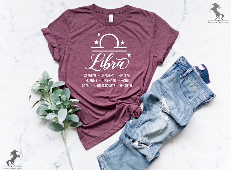 Pu&ograve; includere: Una maglietta color borgogna con un segno zodiacale Bilancia bianco e le parole "Creativo - Affascinante - Pacifico, Amichevole - Diplomatico - Sociale, Leale - Compassionevole - Sensibile".