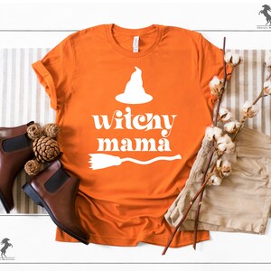May include: Orange t-shirt with a white witch hat, broom, and the text "witchy mama" in a retro font.