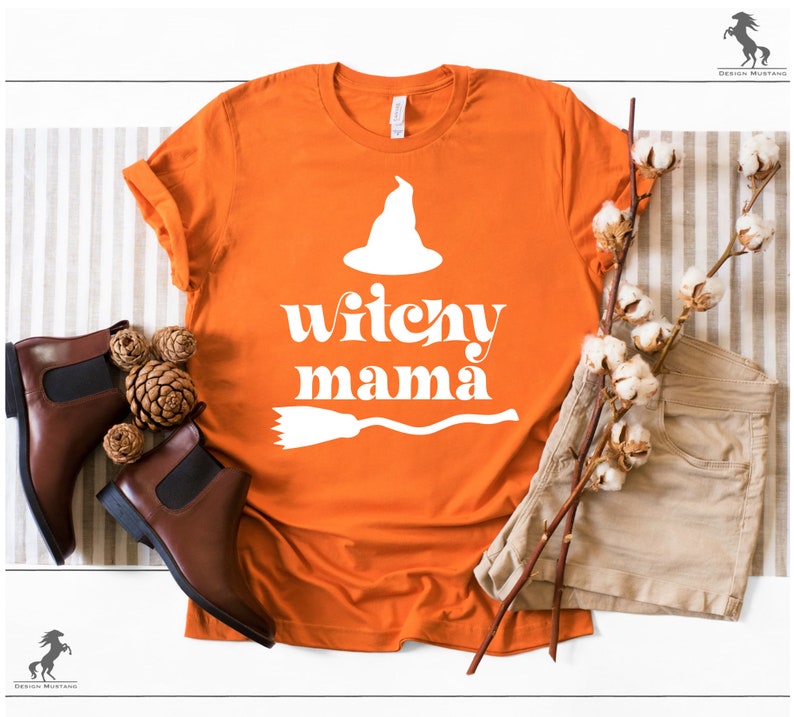 May include: Orange t-shirt with a white witch hat, broom, and the text "witchy mama" in a retro font.